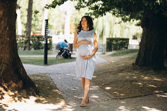 Pregnant woman walking in park, hand on belly, sunny day, trees around. Pregnant woman walking in park, hand on belly, sunny day, trees around.