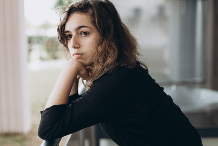 Woman in black shirt, pensive expression, leaning on railing, representing friendship challenges and personal news. Woman in black shirt, pensive expression, leaning on railing, representing friendship challenges and personal news.