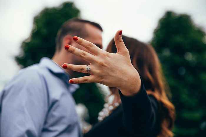 Engaged couple with focus on woman's hand displaying ring, set outdoors with trees in background. Engaged couple with focus on woman's hand displaying ring, set outdoors with trees in background.