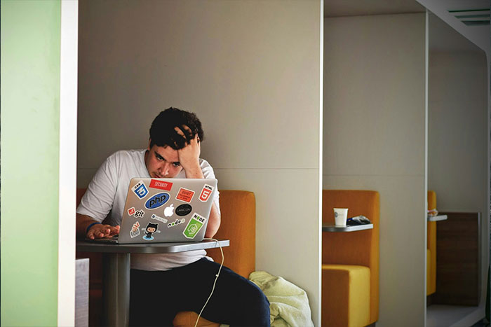 Man looking stressed while using a laptop, covered in tech stickers, in a cafe booth; contemplating ring swap consequences. Man looking stressed while using a laptop, covered in tech stickers, in a cafe booth; contemplating ring swap consequences.