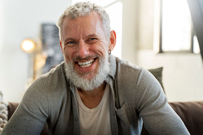 Smiling grown man with a beard wearing a gray cardigan, sitting on a couch in a bright room. Smiling grown man with a beard wearing a gray cardigan, sitting on a couch in a bright room.