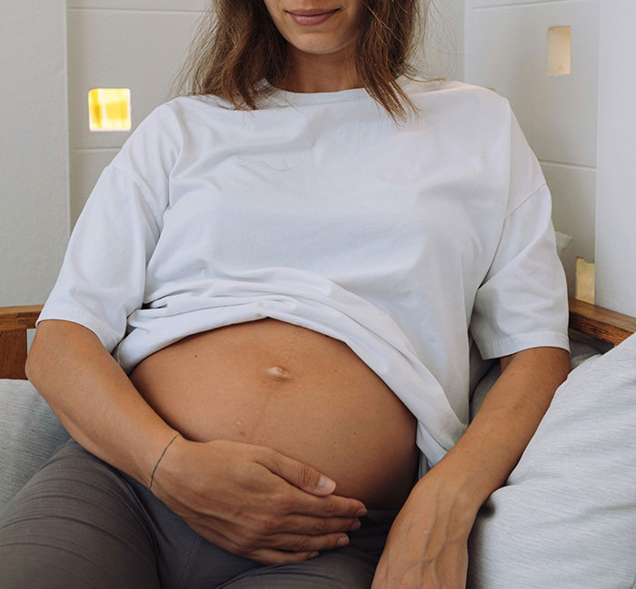 Pregnant woman sitting on a couch, wearing a white shirt, hand on belly. Pregnant woman sitting on a couch, wearing a white shirt, hand on belly.