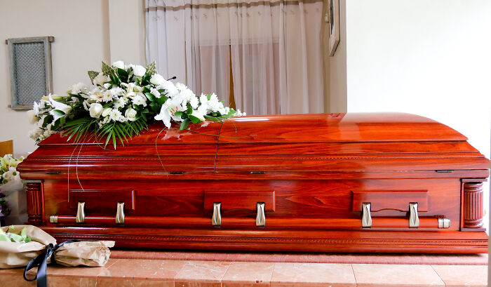 A polished wooden casket with a floral arrangement, a normal societal practice.