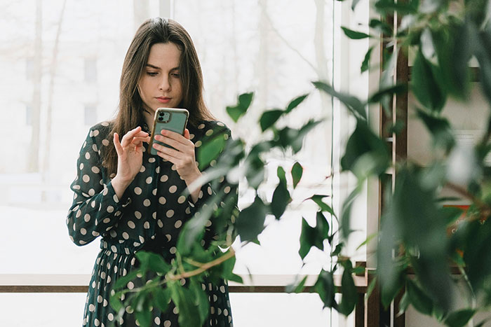 Child-free woman on vacation, using her phone, surrounded by plants, enjoying a peaceful moment indoors. Child-free woman on vacation, using her phone, surrounded by plants, enjoying a peaceful moment indoors.