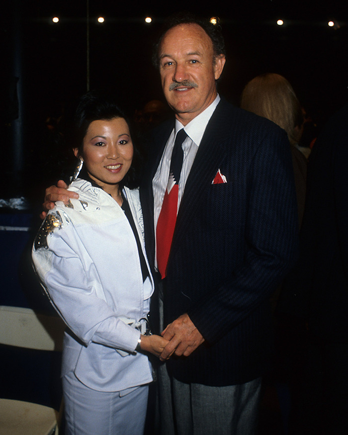 Gene Hackman and Betsy Arakawa posing at an event, man in suit and woman in a white outfit, both smiling. Gene Hackman and Betsy Arakawa posing at an event, man in suit and woman in a white outfit, both smiling.