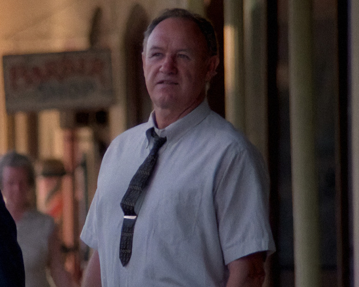 Gene Hackman on a street, wearing a tie and shirt, looks into the distance with a blurred backdrop of a shop sign in a movie scene. Gene Hackman on a street, wearing a tie and shirt, looks into the distance with a blurred backdrop of a shop sign in a movie scene.