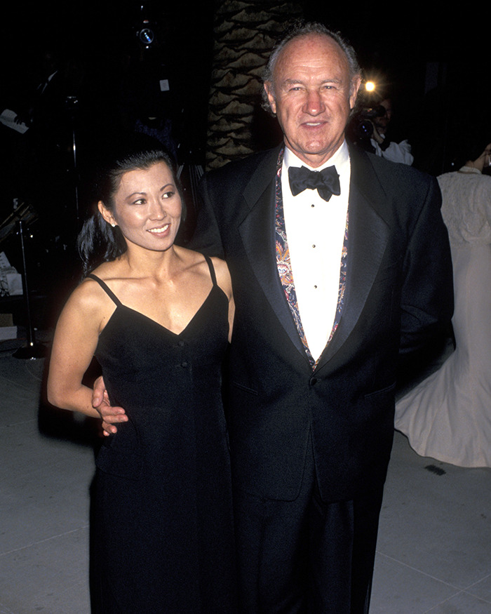 Gene Hackman and Betsy Arakawa in a black dress, poses with a man in formal attire at an event. Gene Hackman and Betsy Arakawa in a black dress, poses with a man in formal attire at an event.