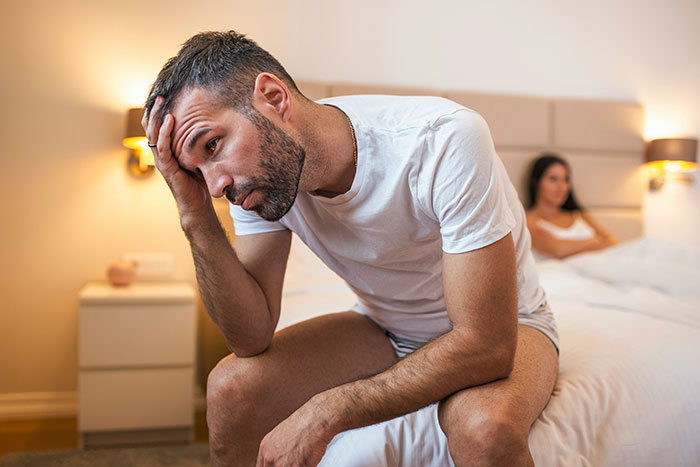 Man looking distressed while sitting on a bed, thinking about a half-naked sauna photo of partner and work spouse. Man looking distressed while sitting on a bed, thinking about a half-naked sauna photo of partner and work spouse.