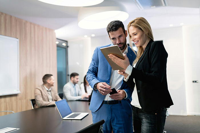 Two colleagues discussing a project in a modern office setting, with others working in the background. Two colleagues discussing a project in a modern office setting, with others working in the background.