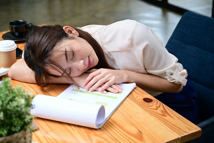 Person asleep on a table at work, highlighting weirdest accepted behaviors in society.