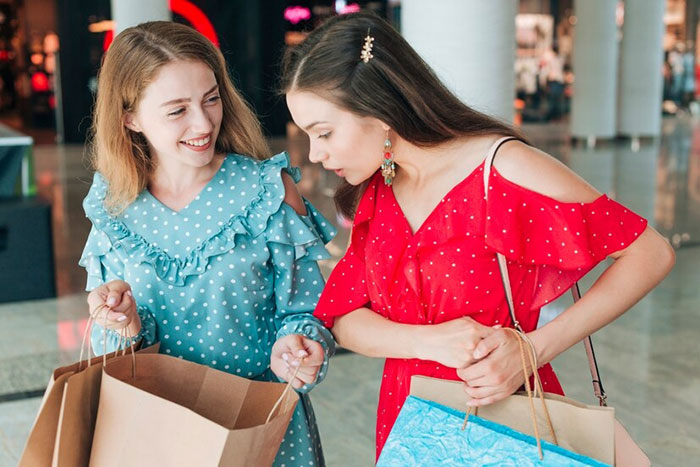 Two teenage girls wearing colorful dresses, smiling while shopping, holding bags in a mall. Two teenage girls wearing colorful dresses, smiling while shopping, holding bags in a mall.
