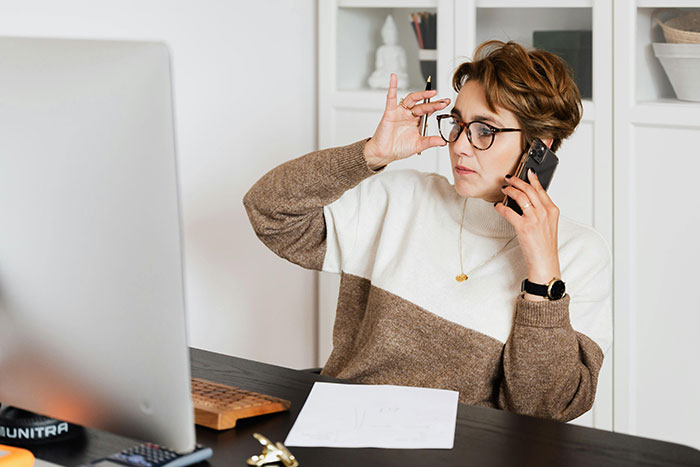 Woman in glasses at desk, holding phone, discussing body-shaming issues related to attention and self-worth. Woman in glasses at desk, holding phone, discussing body-shaming issues related to attention and self-worth.