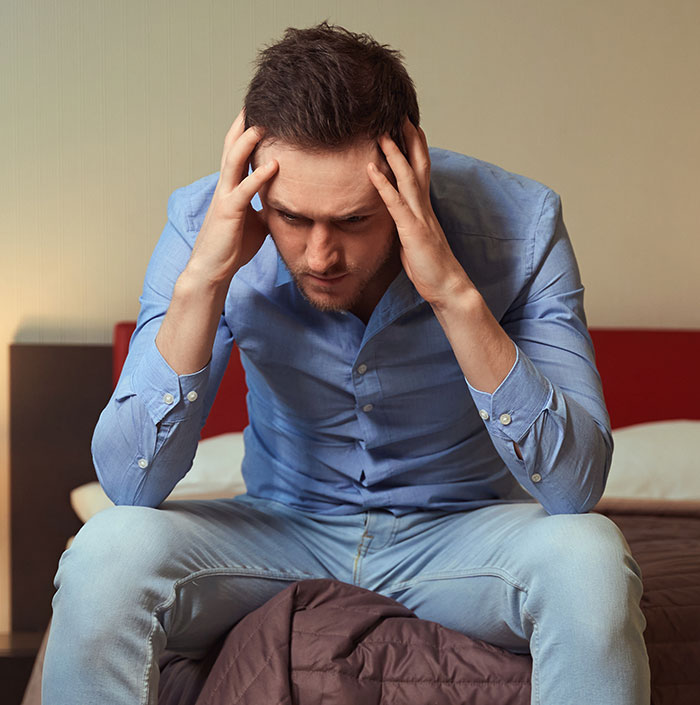Man in a blue shirt sitting on a bed, looking frustrated, concerned about religion and relationship choices. Man in a blue shirt sitting on a bed, looking frustrated, concerned about religion and relationship choices.