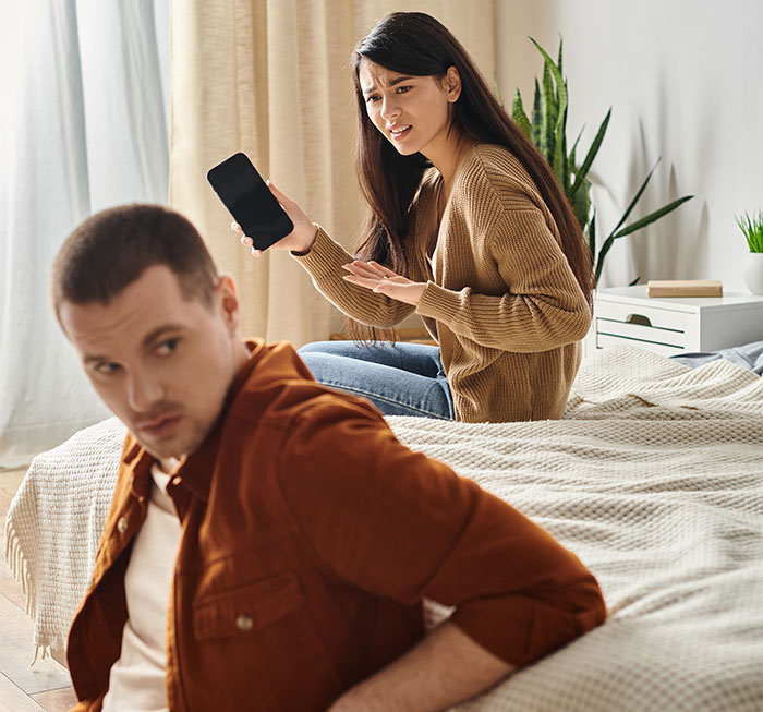 Woman holding a phone argues with man on bed about a photo. Woman holding a phone argues with man on bed about a photo.