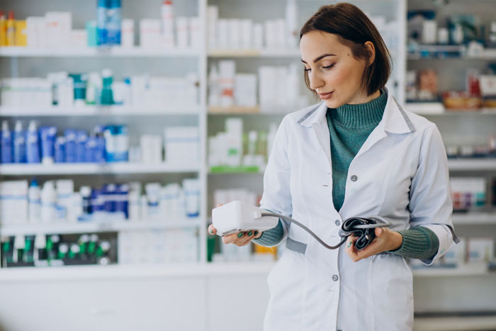 Pharmacy manager in a white coat examining a medical device, surrounded by shelves of medication. Pharmacy manager in a white coat examining a medical device, surrounded by shelves of medication.