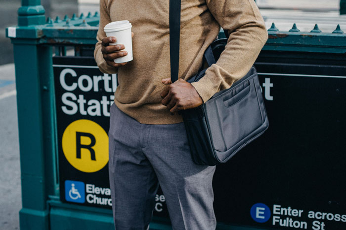 Man holding coffee cup at Cortlandt Street Station entrance, wearing a brown sweater and gray pants, with a black bag. Man holding coffee cup at Cortlandt Street Station entrance, wearing a brown sweater and gray pants, with a black bag.