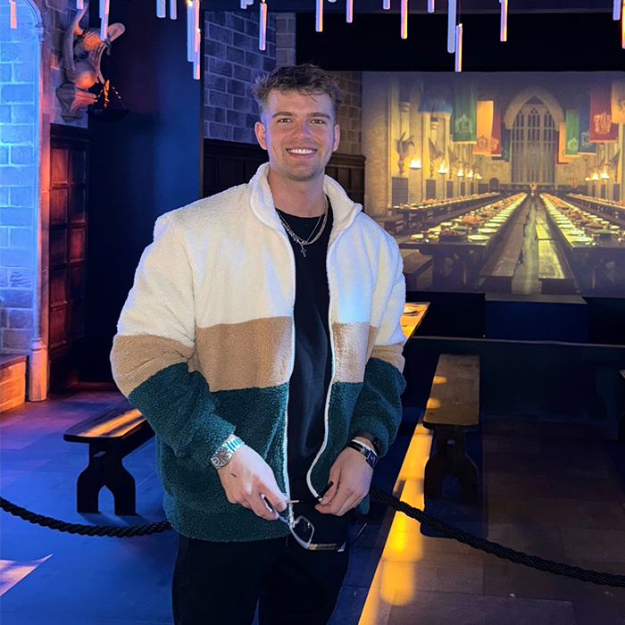 Man smiling in a cozy color-block jacket inside a themed dining hall setting. Man smiling in a cozy color-block jacket inside a themed dining hall setting.