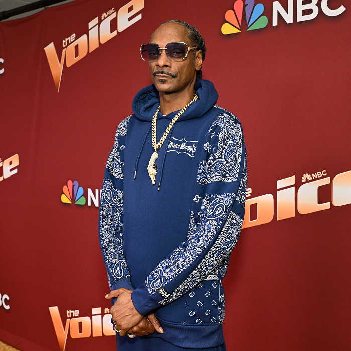 Snoop Dogg in blue bandana-pattern hoodie and sunglasses, standing on "The Voice" red carpet, representing rap royalty and business. Snoop Dogg in blue bandana-pattern hoodie and sunglasses, standing on "The Voice" red carpet, representing rap royalty and business.
