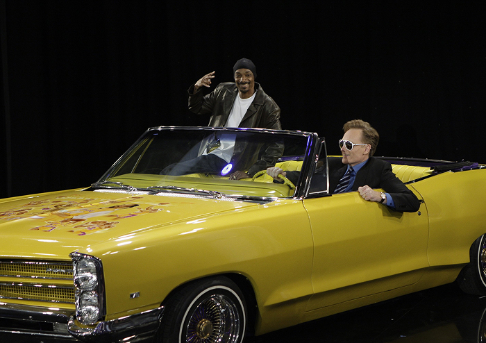 Conan O'Brien posing next to Snoop Dogg in sunglasses driving a yellow car, symbolizing rap royalty and high-stakes lifestyle. Conan O'Brien posing next to Snoop Dogg in sunglasses driving a yellow car, symbolizing rap royalty and high-stakes lifestyle.