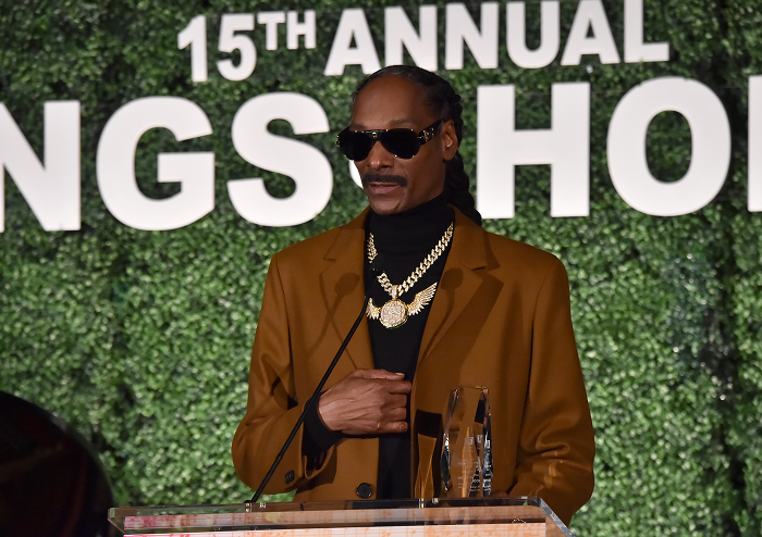 Snoop Dogg in sunglasses and gold chain, speaking at an event, representing rap royalty and business success. Snoop Dogg in sunglasses and gold chain, speaking at an event, representing rap royalty and business success.