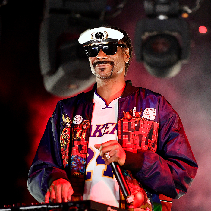 "Snoop Dogg on stage in vibrant jacket and cap, performing under colorful lights. "Snoop Dogg on stage in vibrant jacket and cap, performing under colorful lights.