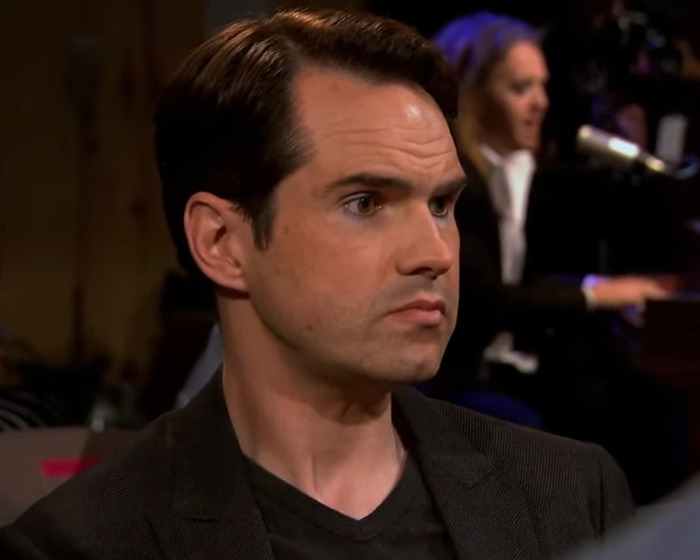Man in a dark blazer with slicked hair, listening intently during a live show, cosmetic tweakments discussion in the background. Man in a dark blazer with slicked hair, listening intently during a live show, cosmetic tweakments discussion in the background.