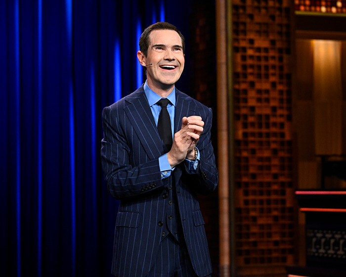 Man in a pinstripe suit on stage, laughing, discussing cosmetic tweaks. Man in a pinstripe suit on stage, laughing, discussing cosmetic tweaks.
