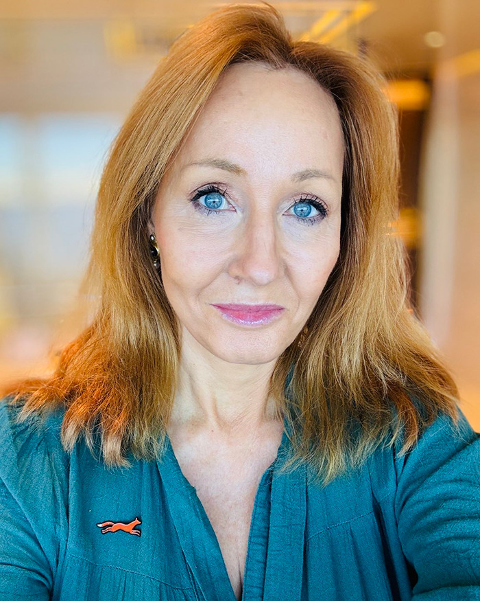 A person with long hair and blue eyes in a room, wearing a green shirt, related to Harry Potter controversy. A person with long hair and blue eyes in a room, wearing a green shirt, related to Harry Potter controversy.