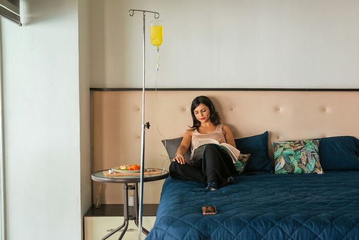 Woman on bed with IV drip, reading a book, highlighting misunderstood healthy practices.