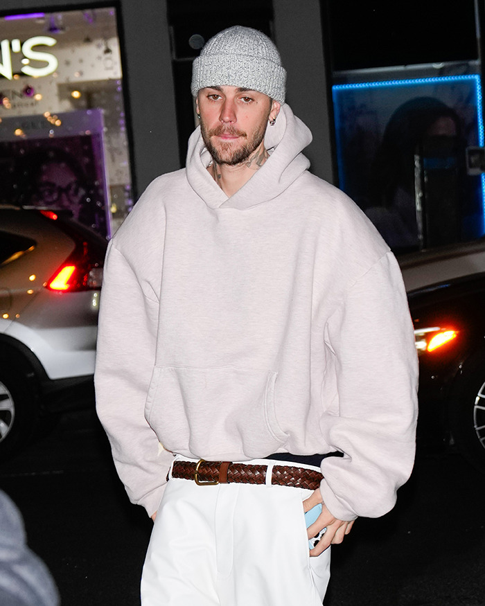 Justin Bieber in a gray beanie and hoodie walking at night. Justin Bieber in a gray beanie and hoodie walking at night.