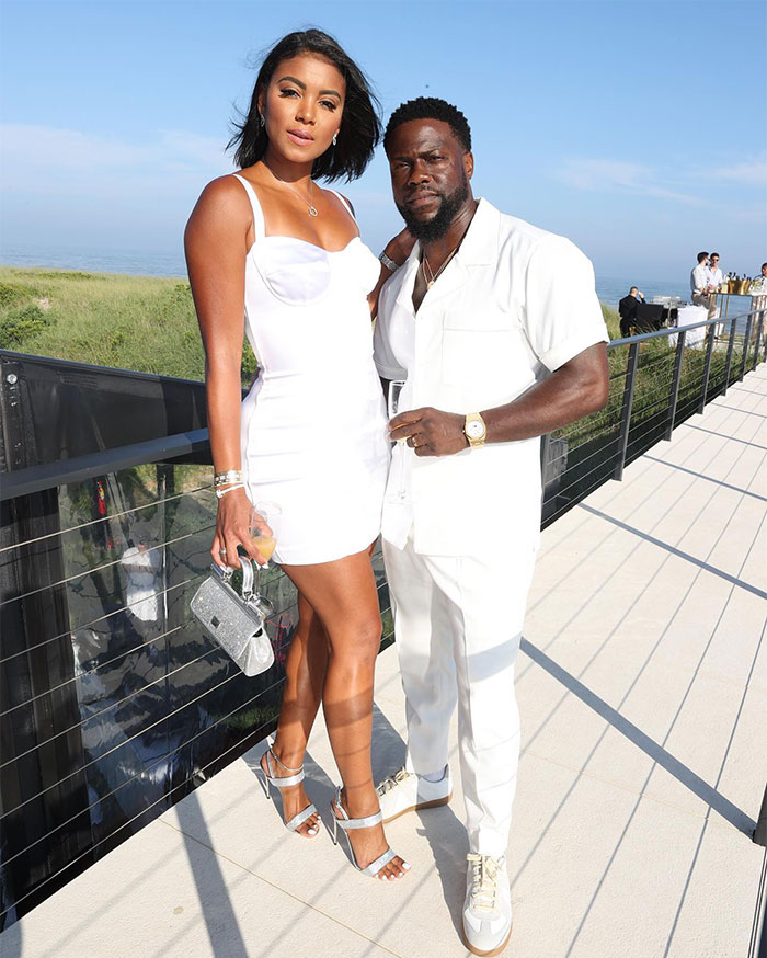 Eniko Hart in a stylish white dress, standing outdoors with Kevin Hart, both dressed for a sunny event. Eniko Hart in a stylish white dress, standing outdoors with Kevin Hart, both dressed for a sunny event.