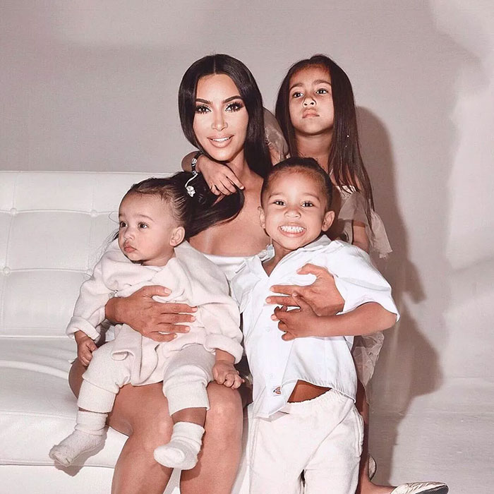 Kim K with her children posing on a white couch, smiling and close together. Kim K with her children posing on a white couch, smiling and close together.