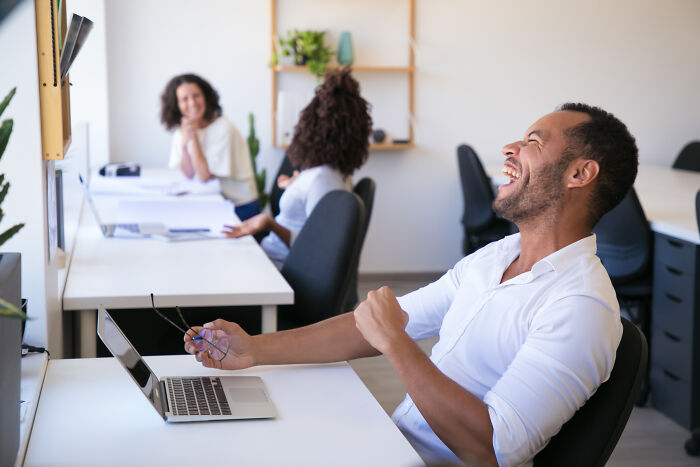 Man laughing at a desk after an April Fools' prank in a bright office setting.