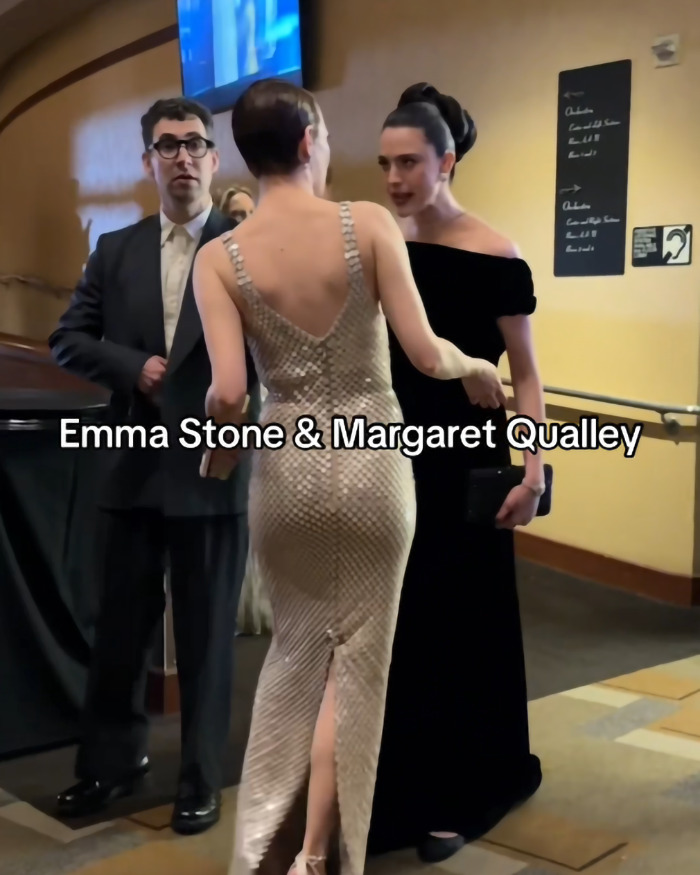 Emma Stone and Margaret Qualley in an animated exchange at an event, attended by a suited gentleman in the background. Emma Stone and Margaret Qualley in an animated exchange at an event, attended by a suited gentleman in the background.