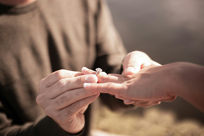Hands exchanging a diamond ring outdoors, symbolizing an engagement or wedding commitment. Hands exchanging a diamond ring outdoors, symbolizing an engagement or wedding commitment.