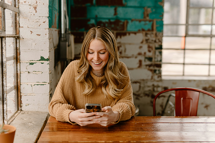 Woman smiling at her phone in a cozy cafe setting, representing a moment of relief after leaving a friend's chaotic wedding plans. Woman smiling at her phone in a cozy cafe setting, representing a moment of relief after leaving a friend's chaotic wedding plans.
