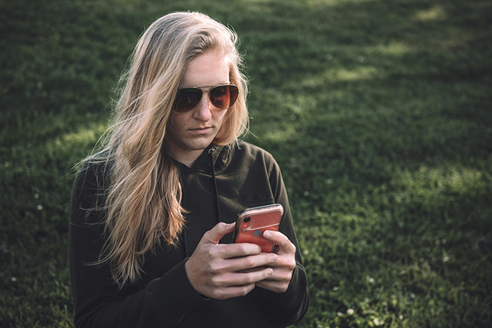 Woman in sunglasses sitting on grass, focused on her phone, amid wedding drama. Woman in sunglasses sitting on grass, focused on her phone, amid wedding drama.