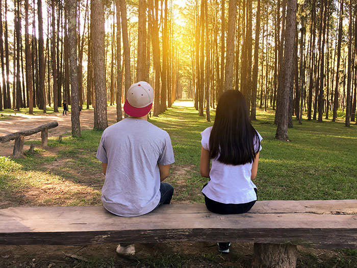 Couple sitting on bench in forest, sunlight filtering through trees, illustrating real love story dynamics. Couple sitting on bench in forest, sunlight filtering through trees, illustrating real love story dynamics.