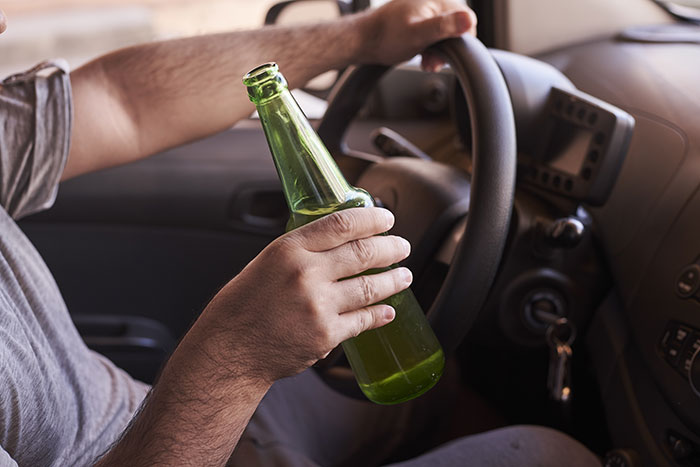 Person holding a green bottle while driving, illustrating a lost license scenario. Person holding a green bottle while driving, illustrating a lost license scenario.