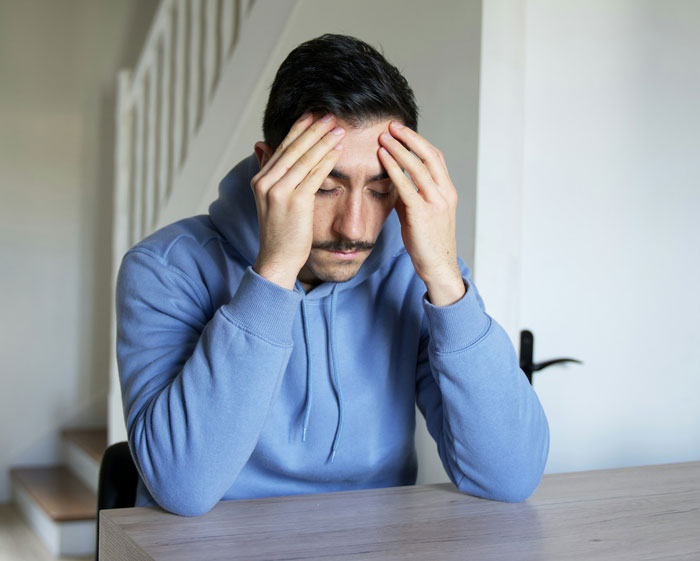 Person in a blue hoodie looking stressed, sitting with head in hands. Person in a blue hoodie looking stressed, sitting with head in hands.