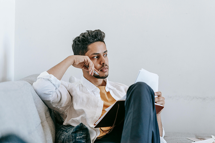 Man sitting on sofa looking thoughtful, holding papers, contemplating end of free rides to work. Man sitting on sofa looking thoughtful, holding papers, contemplating end of free rides to work.