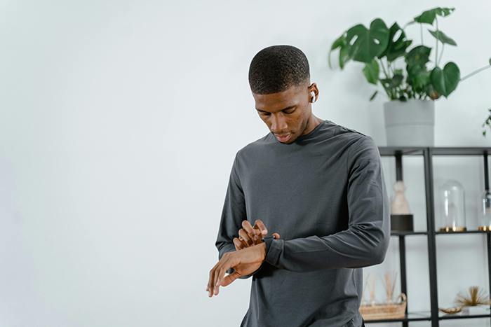 Man checking his watch, wearing earbuds, standing in a room with plants; concept of punctuality and free rides. Man checking his watch, wearing earbuds, standing in a room with plants; concept of punctuality and free rides.