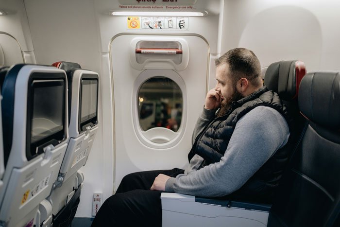 Man sitting by airplane window, looking thoughtful, wearing a black vest, related to "woman made 3 men move" scenario. Man sitting by airplane window, looking thoughtful, wearing a black vest, related to "woman made 3 men move" scenario.