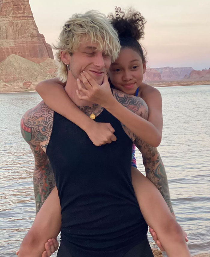 Man with tattoos carries child on his back near a scenic lake, embodying the playful essence of "Celestial Seed. Man with tattoos carries child on his back near a scenic lake, embodying the playful essence of "Celestial Seed.