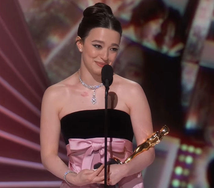 Young woman holding an Oscar statue, wearing a pink and black gown, standing at a microphone on stage. Young woman holding an Oscar statue, wearing a pink and black gown, standing at a microphone on stage.