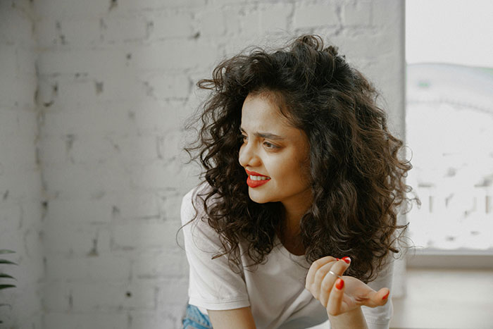 A woman with curly hair in a white shirt, smiling and gesturing, in a casual setting. A woman with curly hair in a white shirt, smiling and gesturing, in a casual setting.