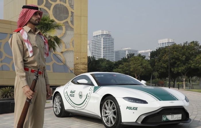 Officer in traditional attire beside luxury police car, linked to model's assault and trafficking investigation. Officer in traditional attire beside luxury police car, linked to model's assault and trafficking investigation.