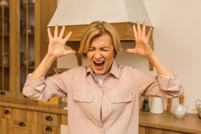A woman in a kitchen showing frustration with her hands raised and eyes closed. A woman in a kitchen showing frustration with her hands raised and eyes closed.