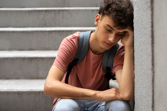 Teen boy sitting on steps, appearing thoughtful and concerned, related to late wife's pictures issue. Teen boy sitting on steps, appearing thoughtful and concerned, related to late wife's pictures issue.