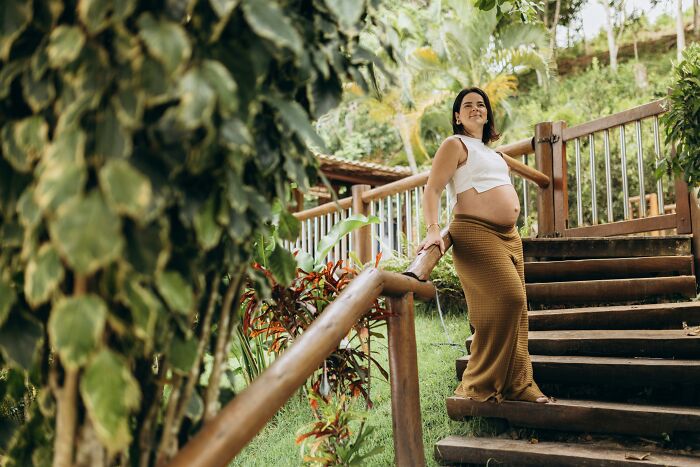 Pregnant woman enjoying a garden view, wearing a white top and brown skirt, related to naming twins after a romantic movie couple. Pregnant woman enjoying a garden view, wearing a white top and brown skirt, related to naming twins after a romantic movie couple.